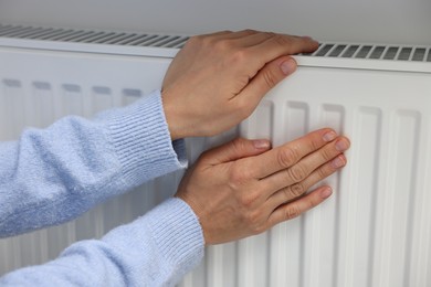 Photo of Woman warming hands near heating radiator indoors, closeup
