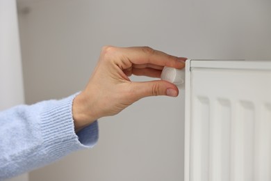 Photo of Woman adjusting temperature of heating radiator indoors, closeup