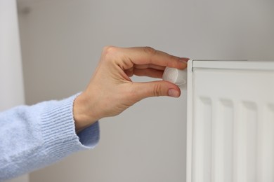 Woman adjusting temperature of heating radiator indoors, closeup