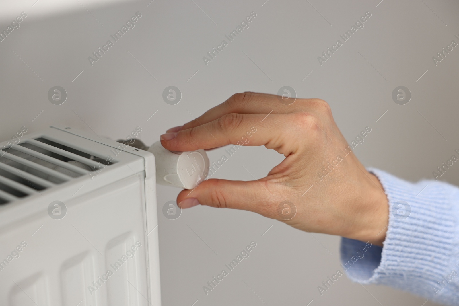 Photo of Woman adjusting temperature of heating radiator indoors, closeup