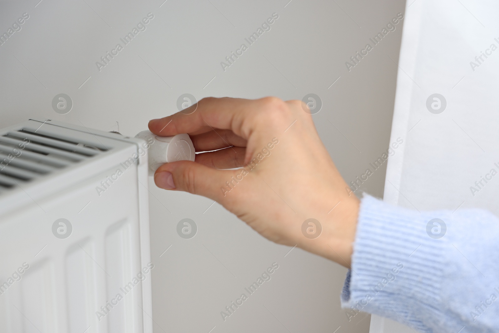 Photo of Woman adjusting temperature of heating radiator indoors, closeup