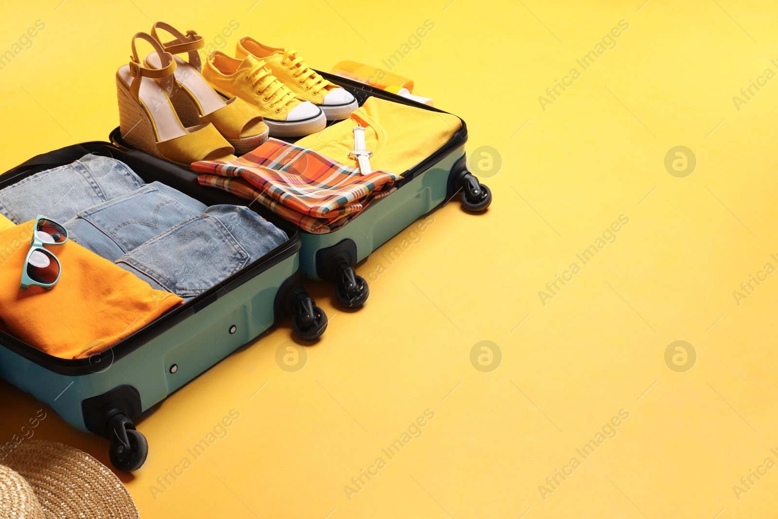 Photo of Open suitcase with traveler's belongings on yellow background, space for text