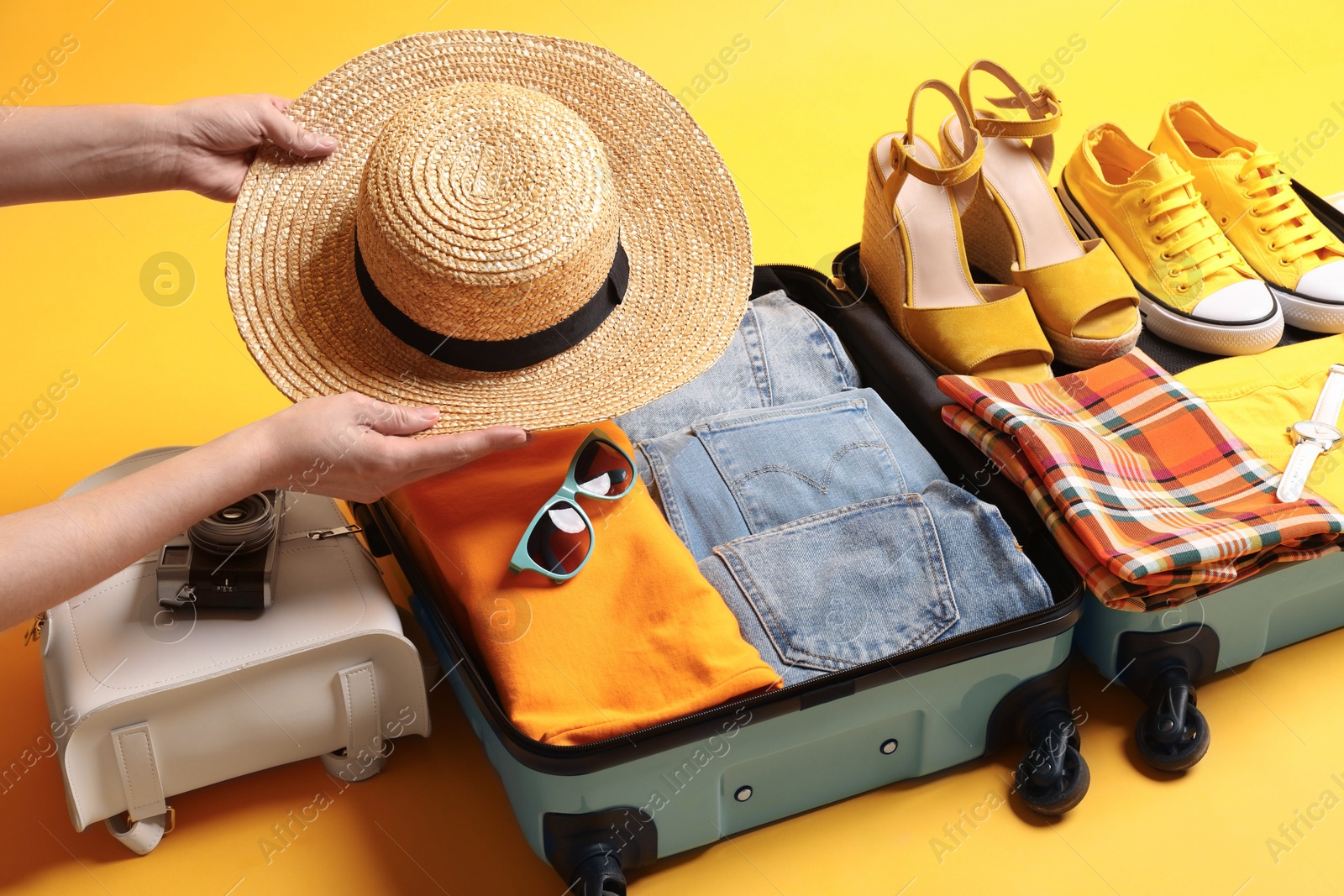 Photo of Woman packing suitcase for trip on yellow background, closeup