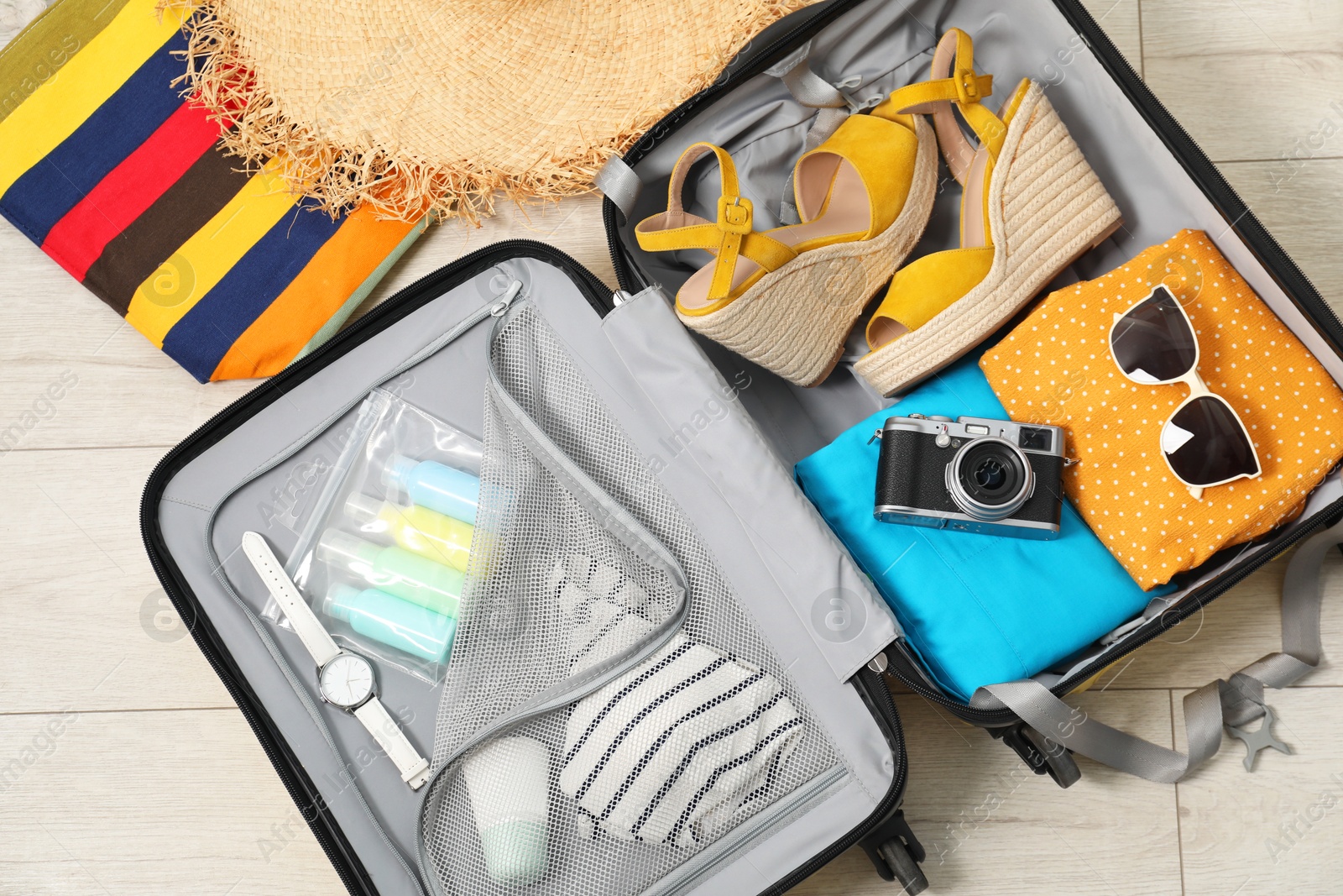 Photo of Open suitcase with traveler's belongings on floor, flat lay