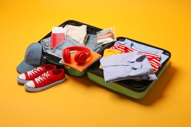 Open suitcase with traveler's belongings on yellow background