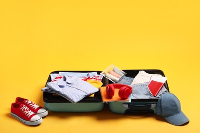 Photo of Open suitcase with traveler's belongings on yellow background, space for text