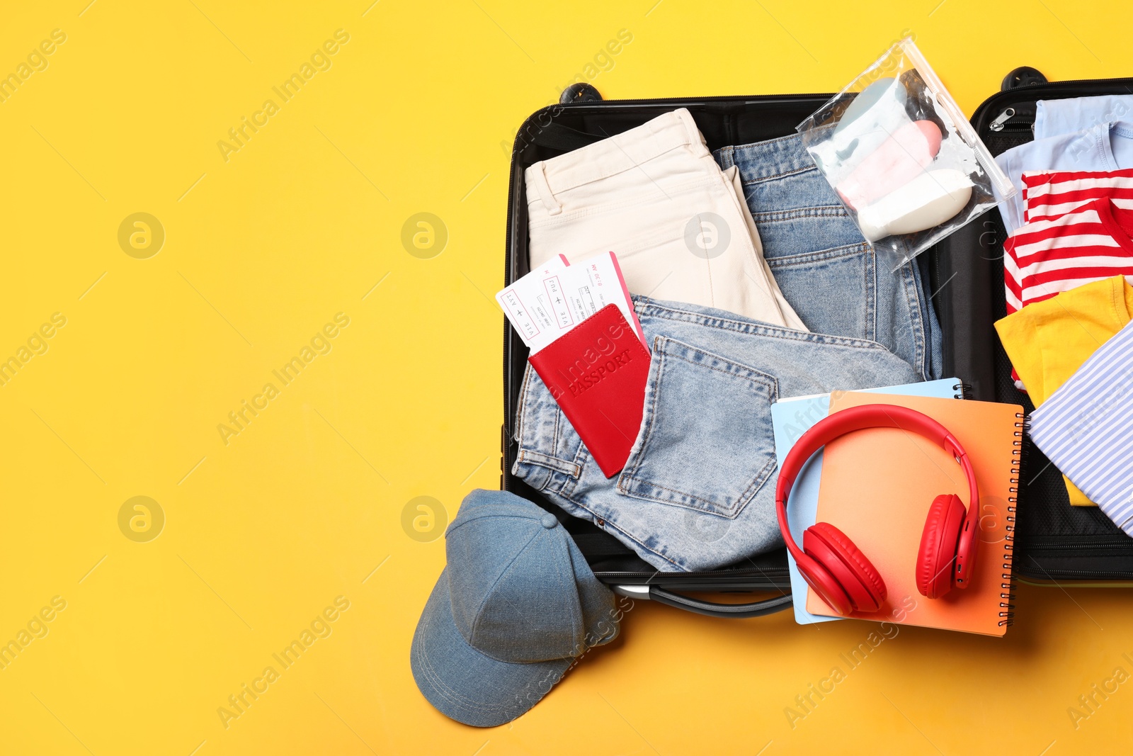 Photo of Open suitcase with traveler's belongings on yellow background, flat lay. Space for text