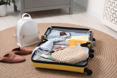 Photo of Open suitcase with traveler's belongings on rug