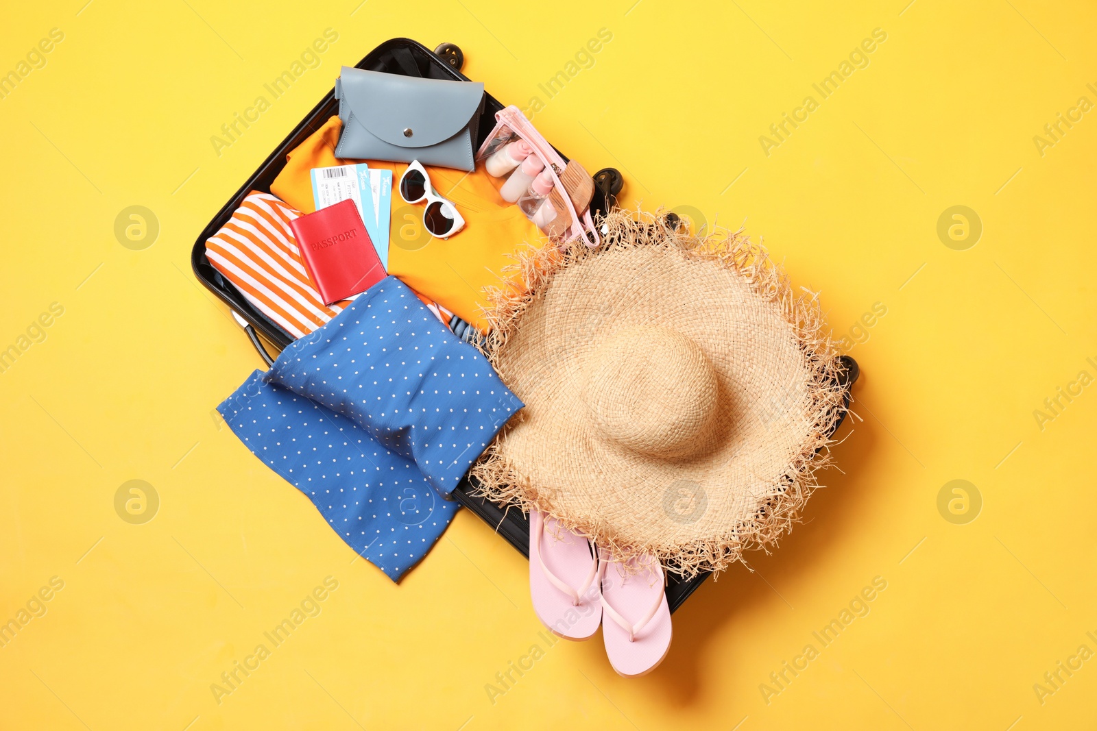 Photo of Open suitcase with traveler's belongings on yellow background, top view