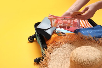 Woman packing suitcase on yellow background, closeup. Space for text