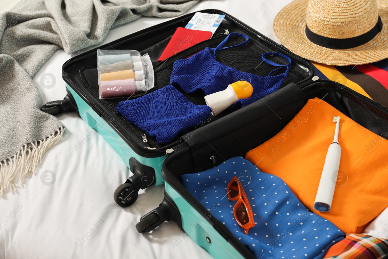 Photo of Open suitcase with traveler's belongings on bed