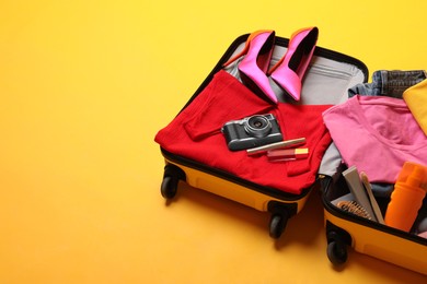 Open suitcase with traveler's belongings on yellow background, space for text