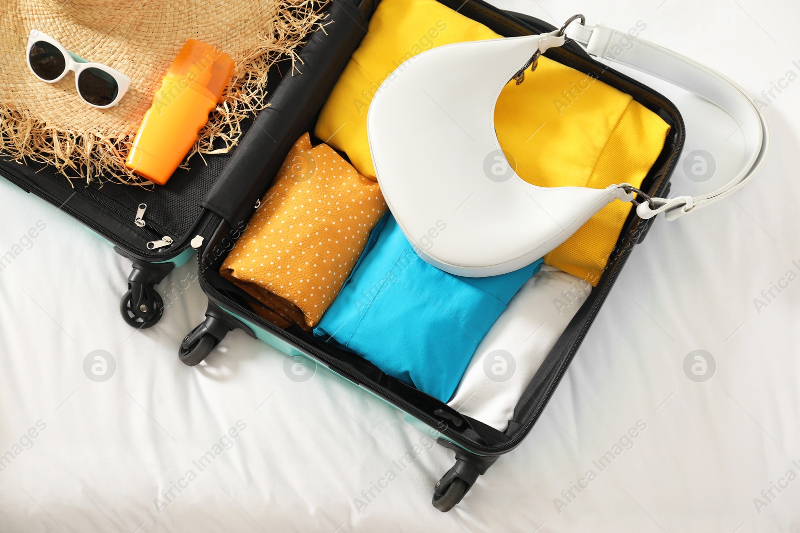 Photo of Open suitcase with traveler's belongings on bed, top view