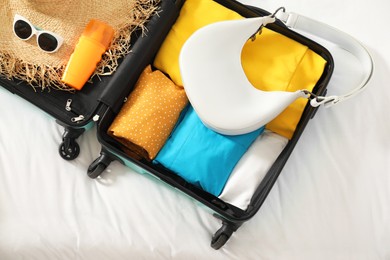 Photo of Open suitcase with traveler's belongings on bed, top view