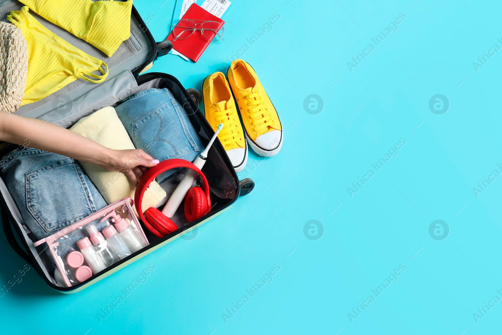 Photo of Woman packing suitcase on light blue background, top view. Space for text