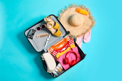 Open suitcase with traveler's belongings on light blue background, flat lay