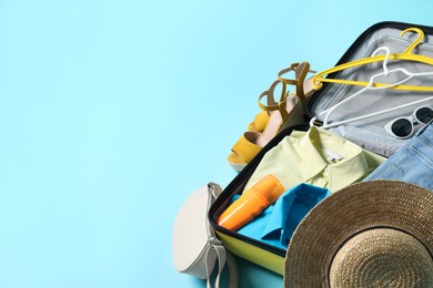 Photo of Open suitcase with traveler's belongings on light blue background, space for text