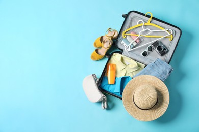 Open suitcase with traveler's belongings on light blue background, flat lay. Space for text