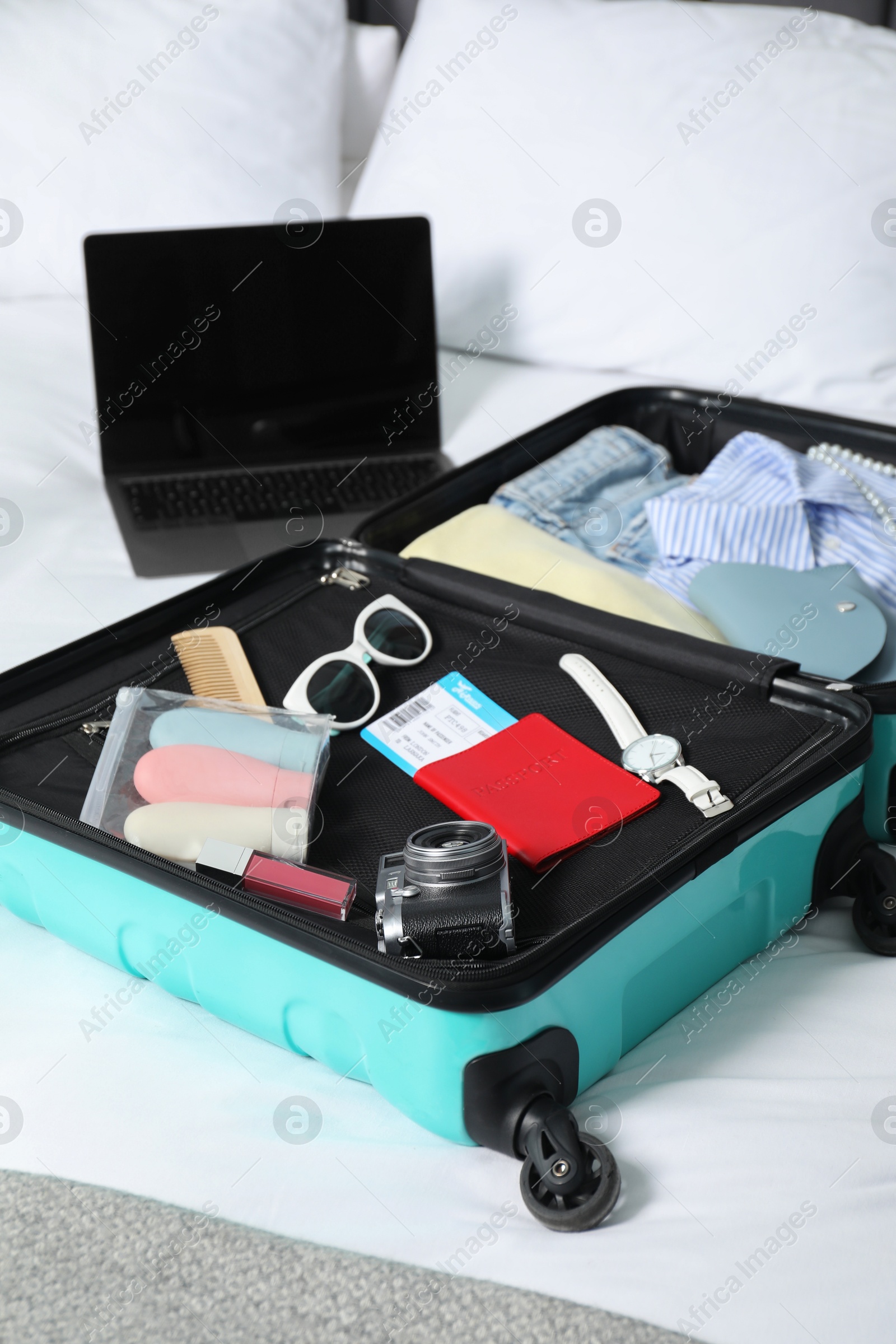 Photo of Open suitcase with traveler's belongings on bed, closeup