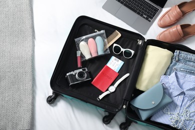 Open suitcase with traveler's belongings on bed, flat lay