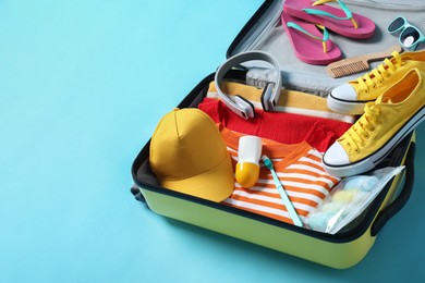 Open suitcase with traveler's belongings on light blue background, space for text