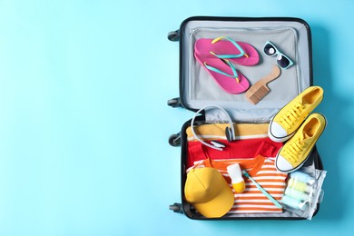 Photo of Open suitcase with traveler's belongings on light blue background, top view. Space for text