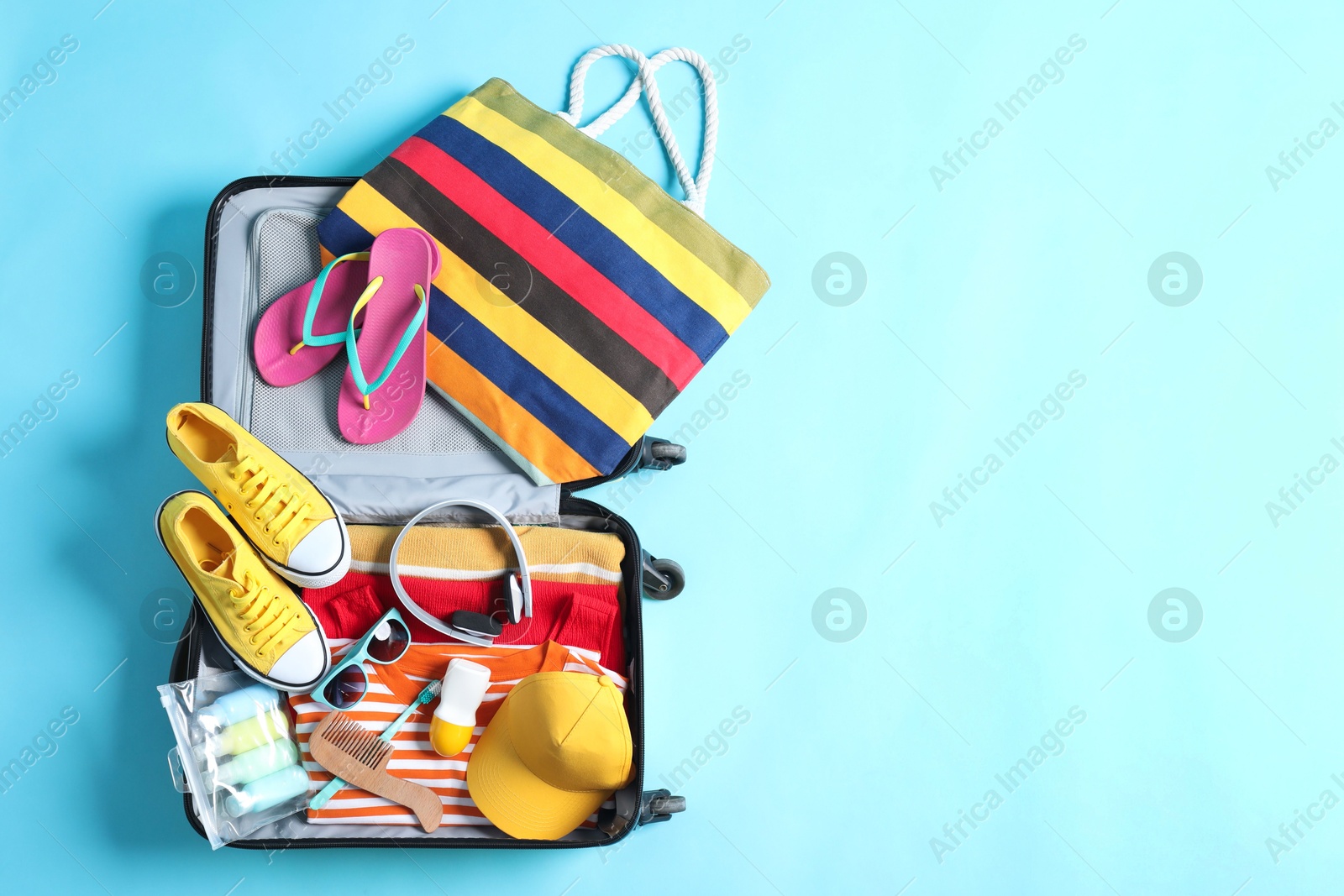 Photo of Open suitcase with traveler's belongings on light blue background, top view. Space for text