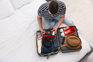 Photo of Man packing suitcase for trip on bed indoors, above view. Space for text
