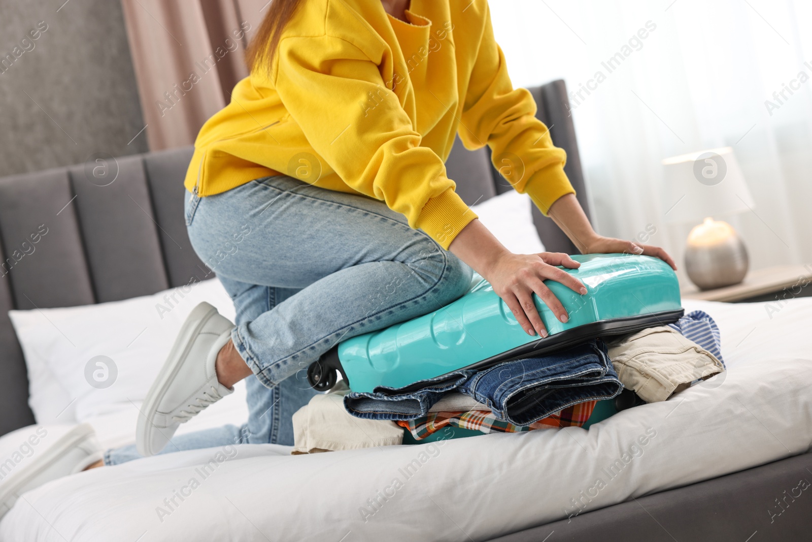 Photo of Woman packing suitcase for trip on bed indoors, closeup