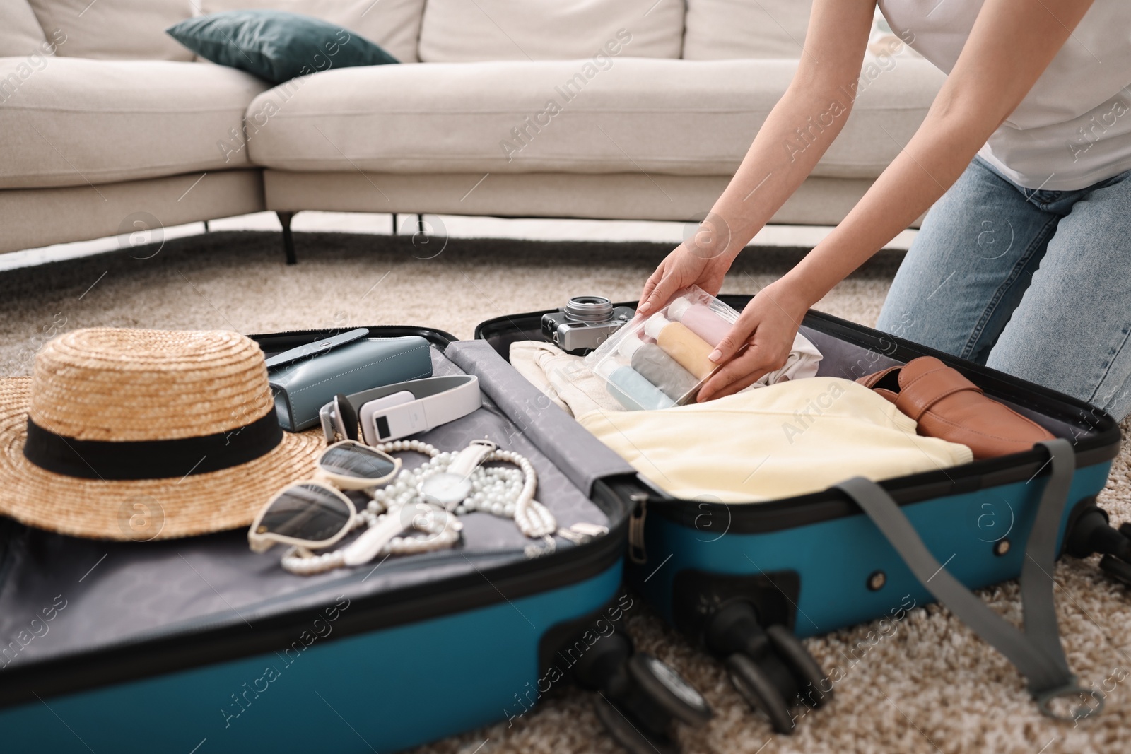 Photo of Woman packing suitcase for trip on floor indoors, closeup