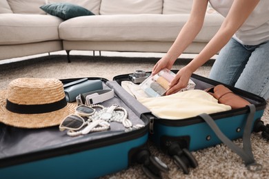 Woman packing suitcase for trip on floor indoors, closeup