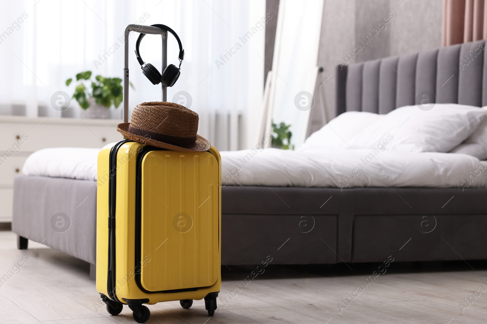 Photo of Yellow suitcase, headphones and straw hat in bedroom