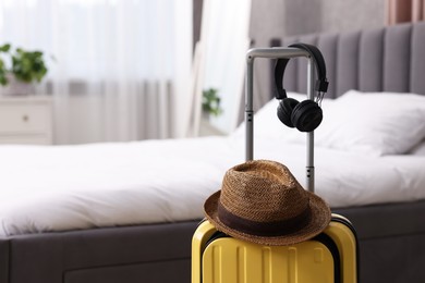 Photo of Yellow suitcase, headphones and straw hat in bedroom