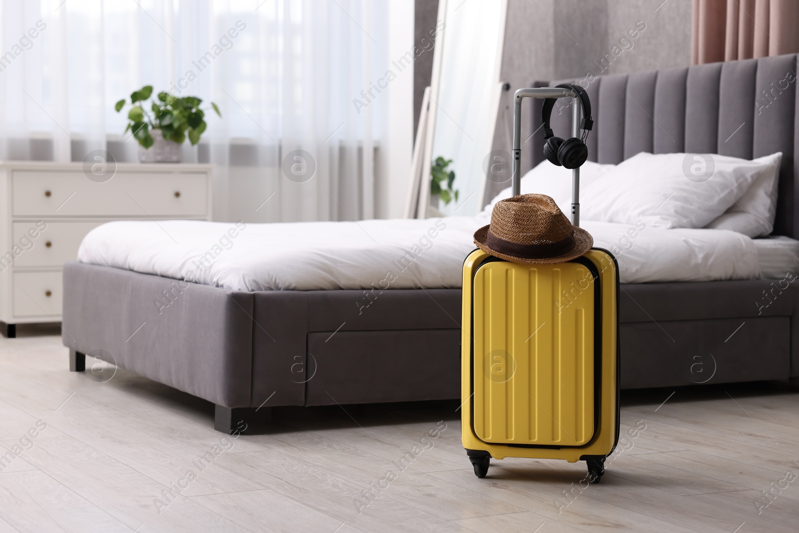 Photo of Yellow suitcase, headphones and straw hat in bedroom