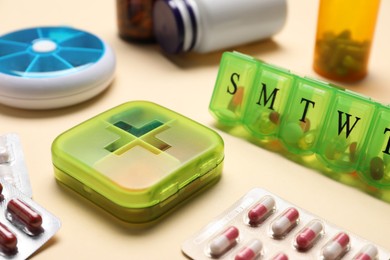 Different pills, organizers and medical jars on beige background, closeup