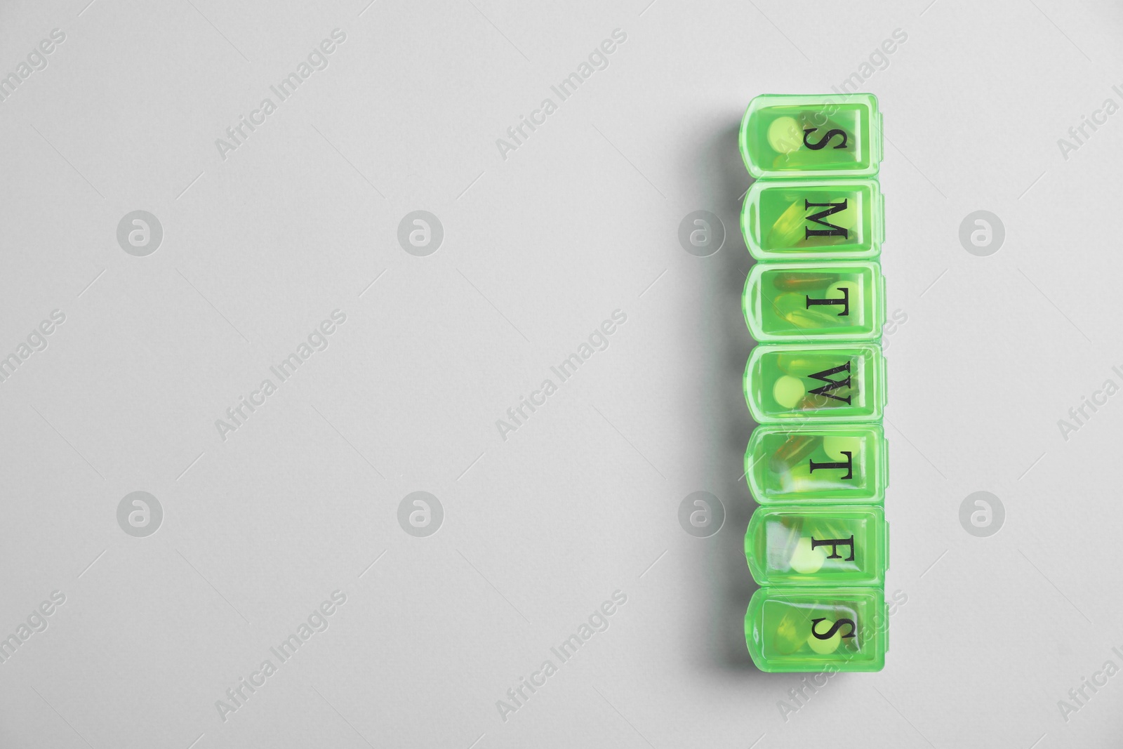 Photo of Different pills in organizer on light background, top view. Space for text