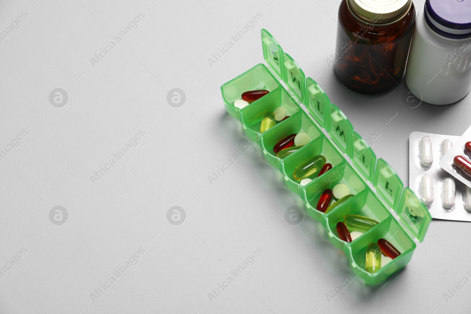 Photo of Different pills, organizer and medical jars on light background, space for text