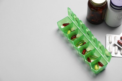 Different pills, organizer and medical jars on light background, space for text