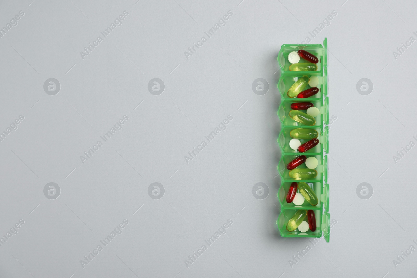 Photo of Different pills in organizer on light background, top view. Space for text