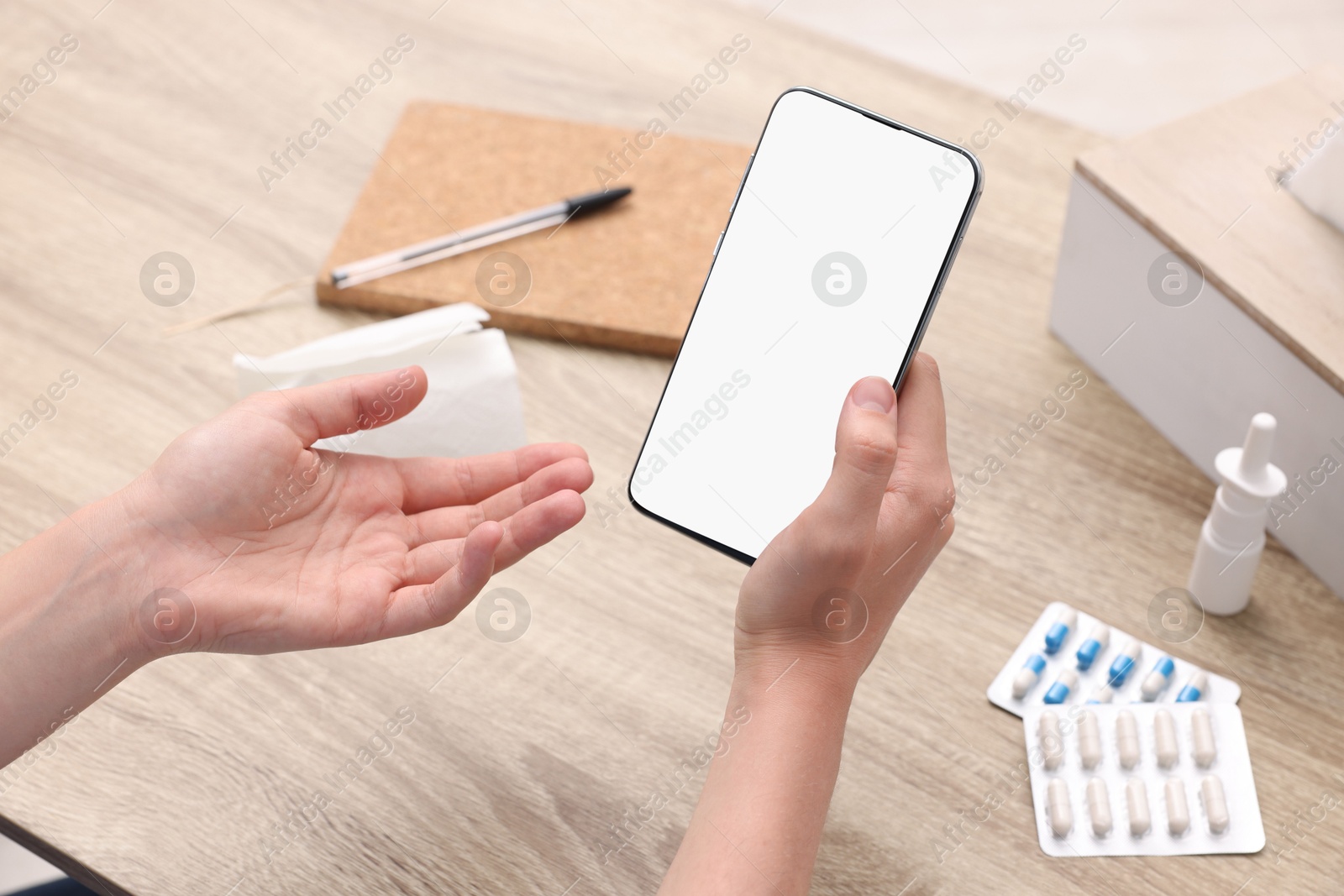 Photo of Sick woman having online consultation with doctor via smartphone at wooden table, closeup