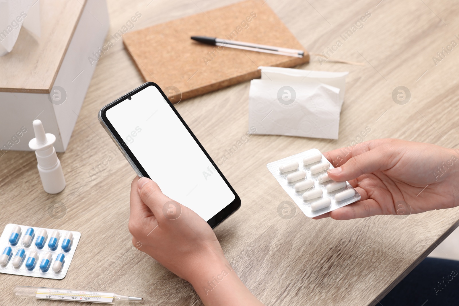 Photo of Sick woman with pills having online consultation with doctor via smartphone at wooden table, closeup