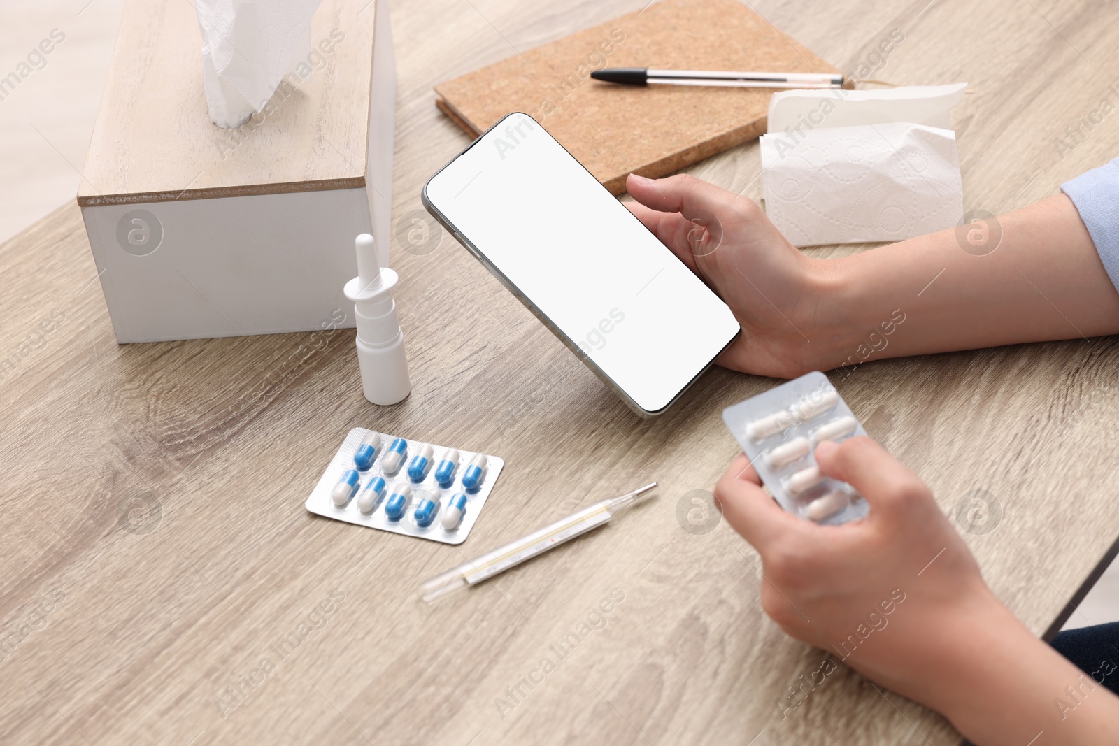 Photo of Sick woman with pills having online consultation with doctor via smartphone at wooden table, closeup