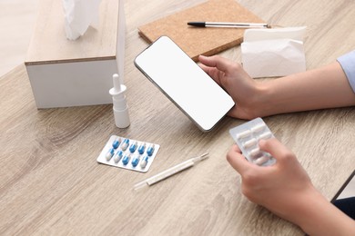 Photo of Sick woman with pills having online consultation with doctor via smartphone at wooden table, closeup