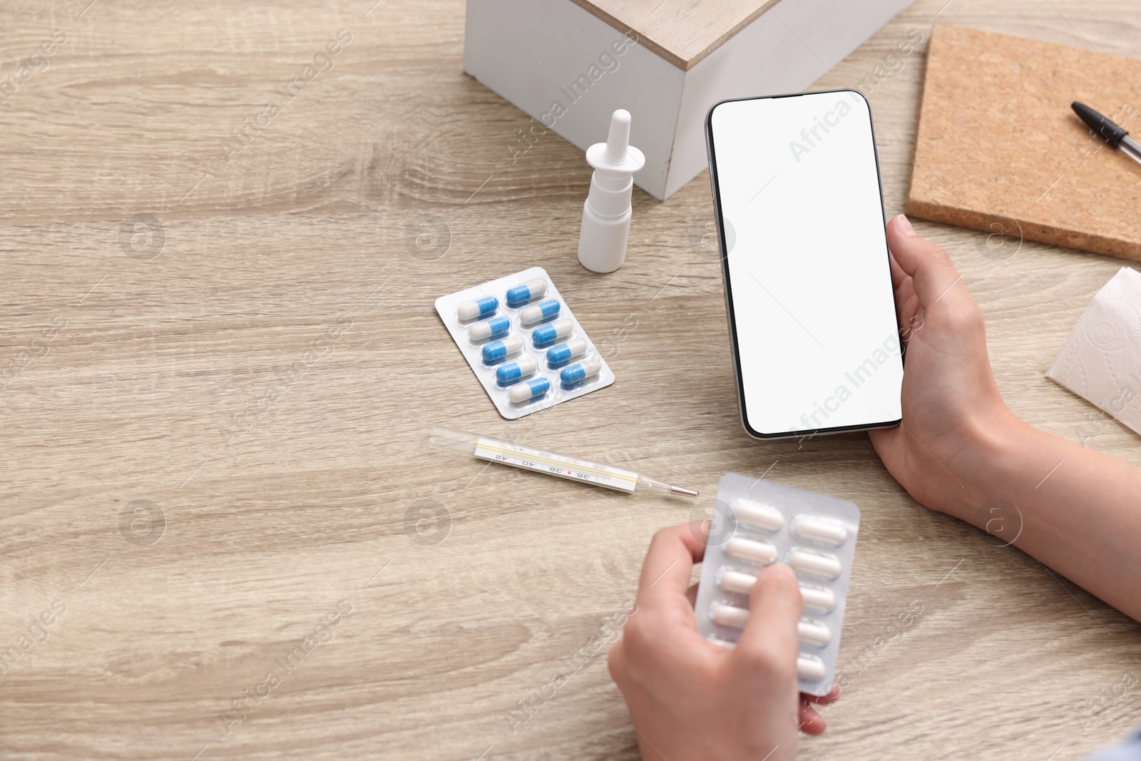 Photo of Sick woman with pills having online consultation with doctor via smartphone at wooden table, closeup