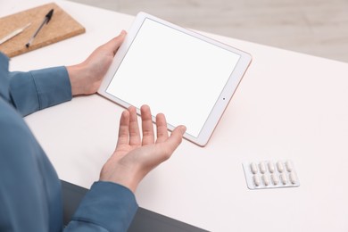 Photo of Sick woman having online consultation with doctor via tablet at white table indoors, closeup