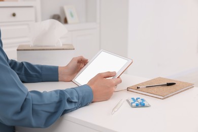 Sick woman having online consultation with doctor via tablet at white table indoors, closeup