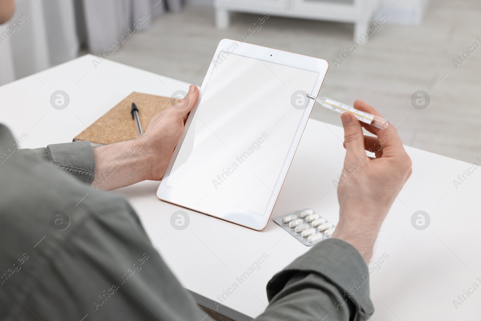 Photo of Sick man with thermometer having online consultation with doctor via tablet at home, closeup