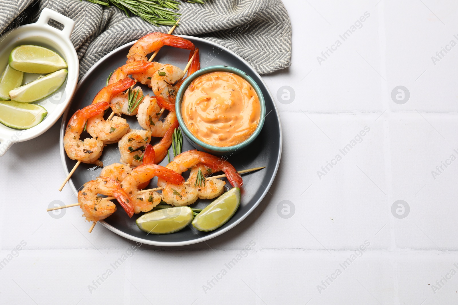 Photo of Skewers with delicious grilled shrimps served on white tiled table, flat lay. Space for text