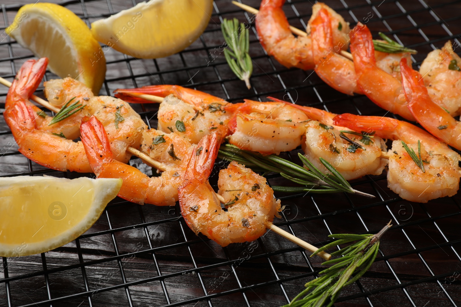 Photo of Skewers with delicious grilled shrimps, herbs and lemon on wooden table, closeup