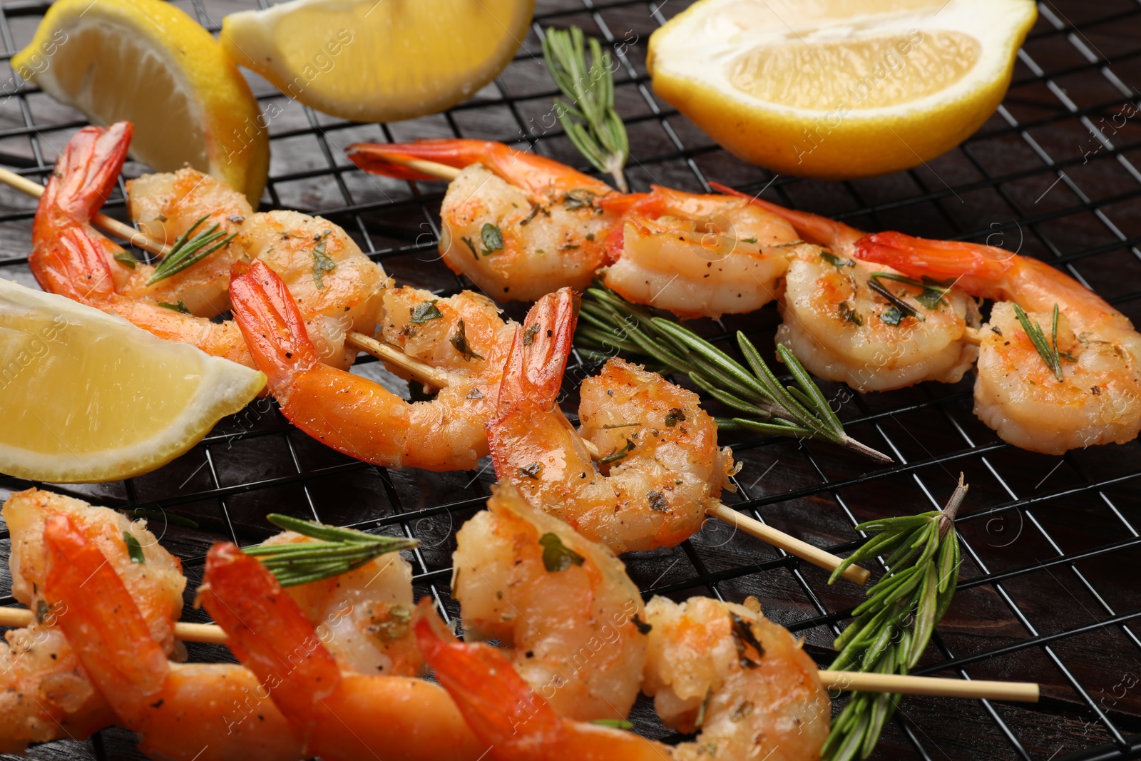 Photo of Skewers with delicious grilled shrimps, herbs and lemon on wooden table, closeup